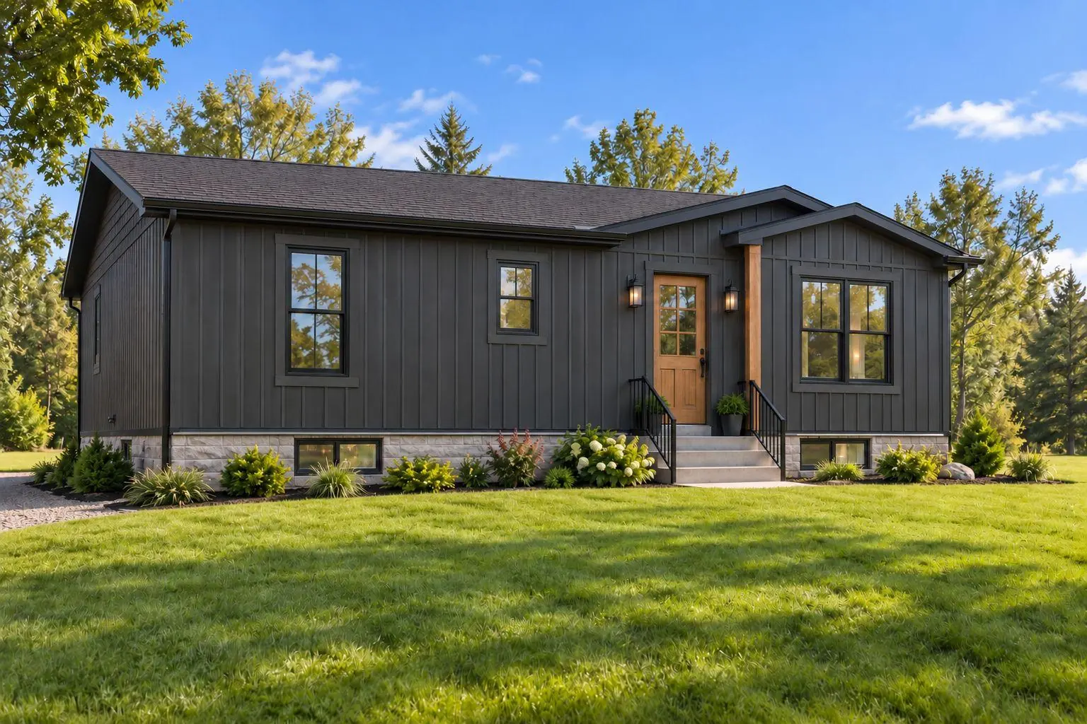 A single storey home with dark board and batten siding, black window frames and a wood front door, on a stone foundation on a mown lawn under a blue sky.