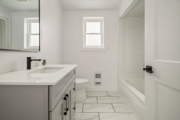 The bathroom of a finished REDI-HOME, with a quartz-topped vanity, marble-effect tile flooring and a tub and shower.