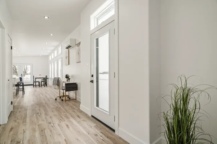 The entry and hallway of a finished REDI-HOME, looking down vinyl plank flooring past a wall-mounted mini-split and a row of transom windows toward the dining area.