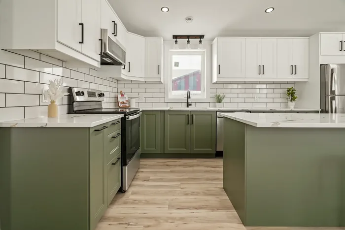 The kitchen straight on, with quartz countertops, sage green lower cabinets, white shaker uppers, a white subway tile backsplash and a window over the sink looking out to the farm.
