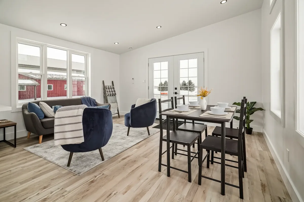 The open living and dining area of a finished REDI-HOME, with a sofa and armchairs at one end, a dining table at the other, and French doors to the yard.