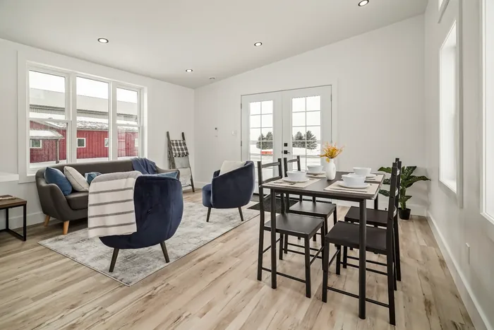 The open living and dining area of a finished REDI-HOME, with a sofa and armchairs at one end, a dining table at the other, and French doors to the yard.
