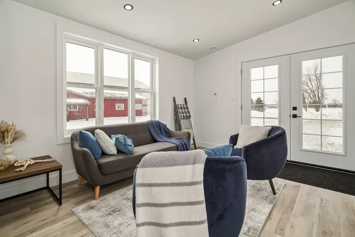 The living area of a finished REDI-HOME, with a wide window looking out to a red barn under snow and French doors to the side.
