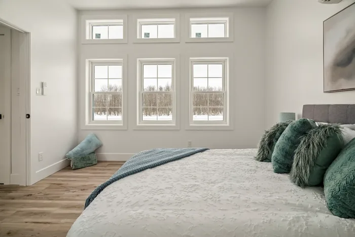 The master bedroom of a finished REDI-HOME, with three windows and transoms above them looking out to snow and bare woodland.