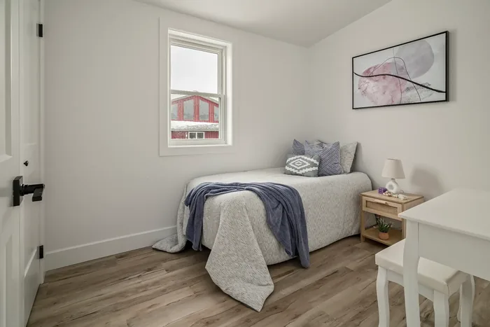 A second bedroom in a finished REDI-HOME, with a single bed, a study desk and a window looking out to the barn.